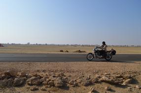 Girl biker on the road in Jaisalmer, India, among the beautiful fields with the rocks