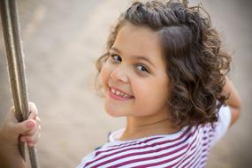 Portrait of the cute child girl, with the curly hair, on the playground