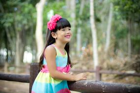 Cute smiling girl with the pink flowers and pink lips, in the colorful dress, near the green trees