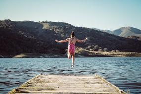 girl in a pink swimsuit jumping into a lake from a pier in California