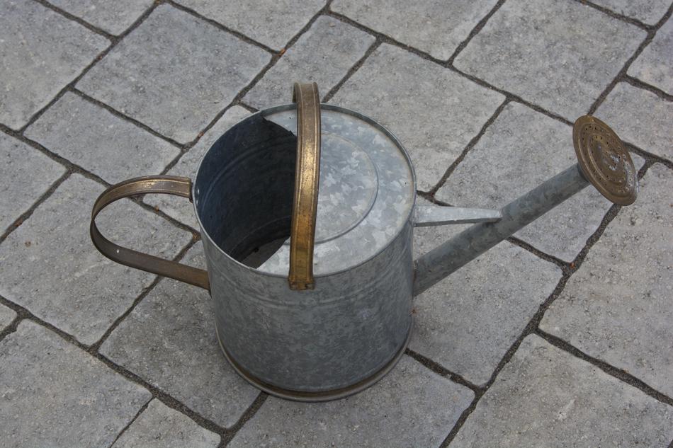 Close-up of the old, shiny watering can on the pavement