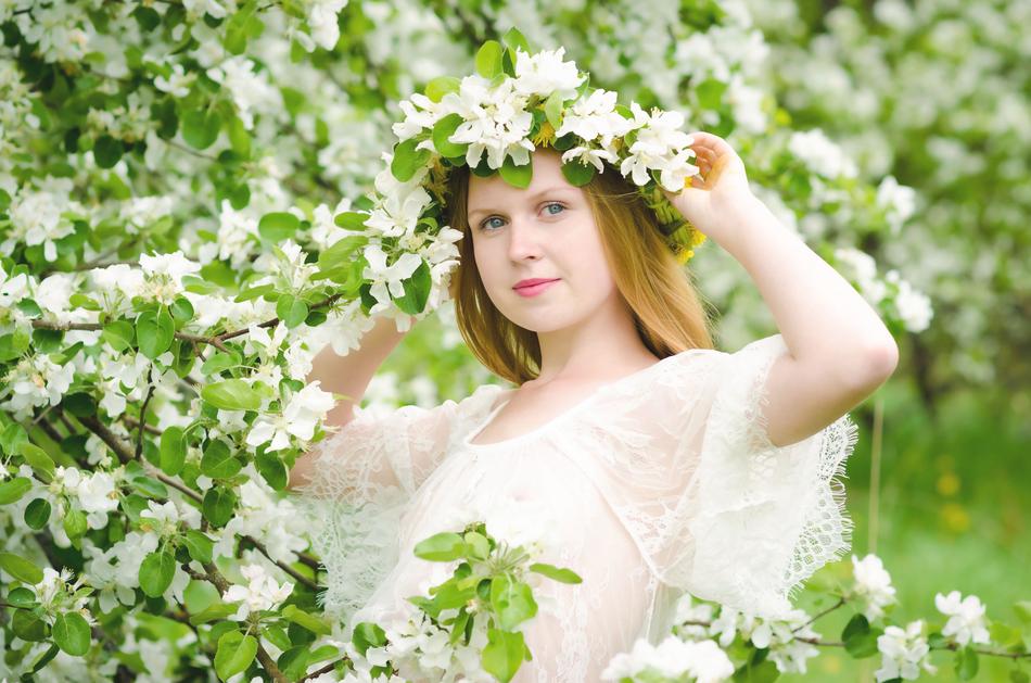 beautiful Girl with wreath on head near apple tree in bloom