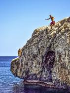 Man, jumping from the colorful cliff, into the water with ripple, at blue sky on background