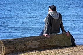 man on a log near the water on a clear day