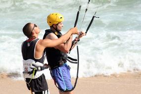 People, on the sandy beach, with the kite surfing equipment, in sunlight