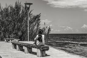 black and white photo of Thoughtful Girl on bench on Sea coast