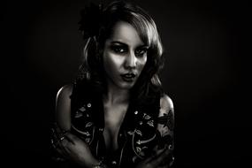 Black and white photo with the portrait of the beautiful girl in vest, at black background