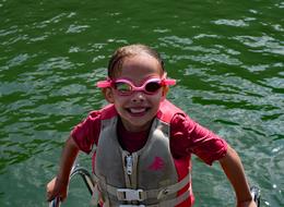 Girl with pink swimming goggles in the green swimming pool