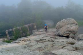 girl runs over large stones in the fog