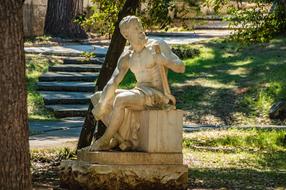 Beautiful statue of the man, among the green plants, in sunlight and shadows, in the park