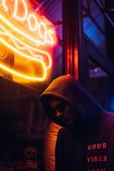 Person in hood and with sunglasses near the beautiful, bright, neon sign of Hot Dogs