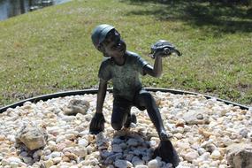 Beautiful, shiny, statue of the boy, with the turtle, among the stones and colorful grass