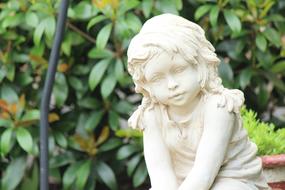 Beautiful, white statue of the girl Angel, among the colorful plants in the garden