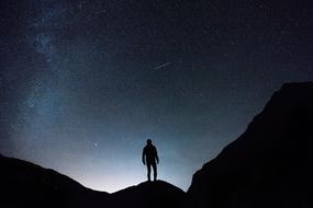 silhouette of man standing on rock at starry sky