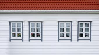 White and red house with the windows with curtains, and colorful flowers inside