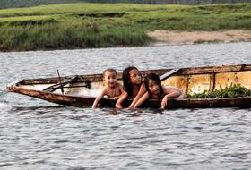 Children on the boat, among the river with ripple, near the shore with green grass