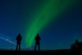 silhouettes of people on the background of green northern lights