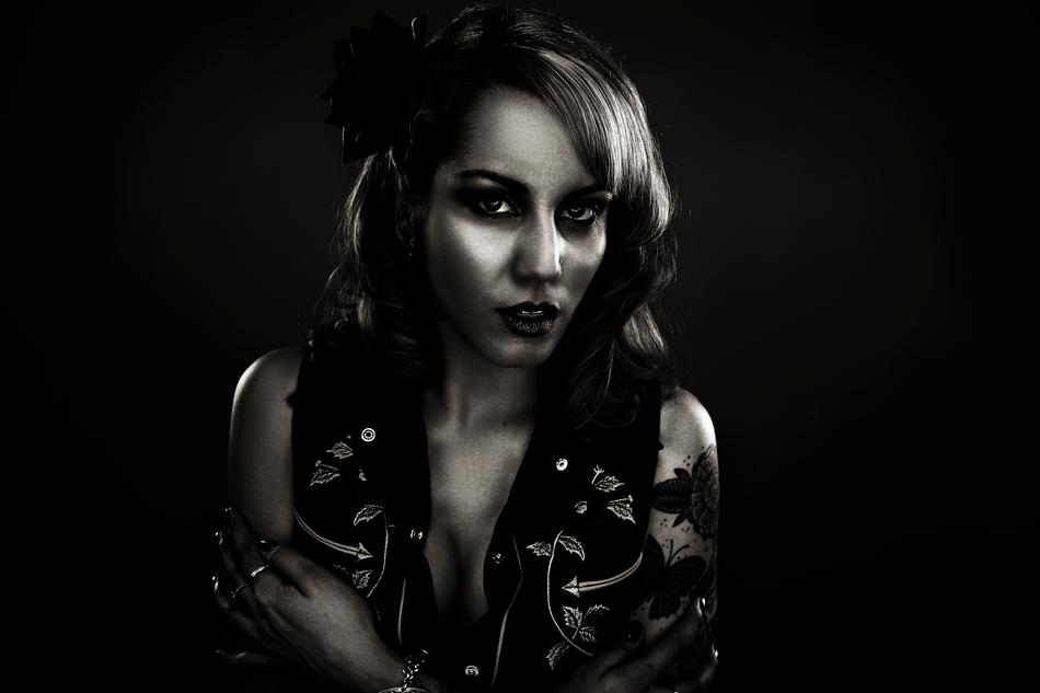Black and white photo with the portrait of the beautiful girl in vest, at black background