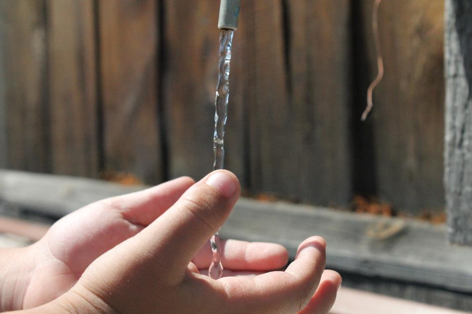 Baby, washing hands with the water, near the wooden fence