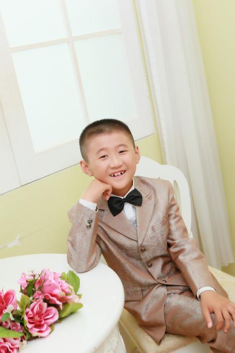 Smiling boy in suit with the bow tie, near the colorful and beautiful flowers on the round table
