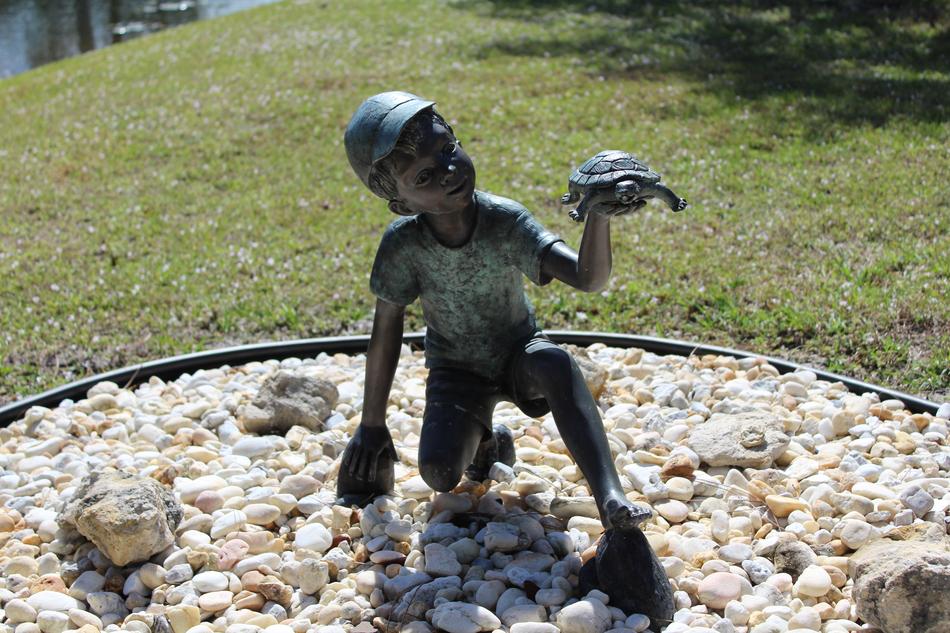 Beautiful, shiny, statue of the boy, with the turtle, among the stones and colorful grass