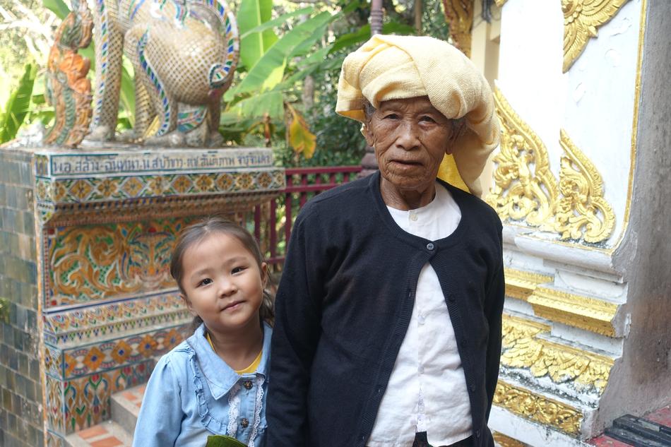 Portrait of the great-grandmother, with the great-granddaughter, near the colorful and beautiful building in Thailand
