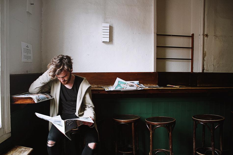 young man reading a newspaper while sitting at the bar