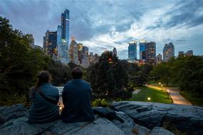 Couple sitting on rock in front of city at dusk