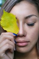 Portrait of the girl holding yellow and green leaf covering her eye