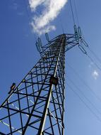 Low angle shot of the electrical tower of the power line, with the cables, in sunlight, under the blue sky with white clouds