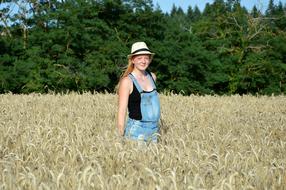 Smiling, blonde girl in hat, among the yellow plants, on the field, near the green plants