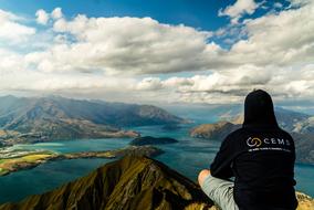 Back view of the man, sitting on the beautiful mountain, near the beautiful turquoise lake, under the blue sky with clouds