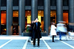 People on the street, in motion, near the building with lights