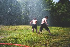 Boys Children playing with water on meadow