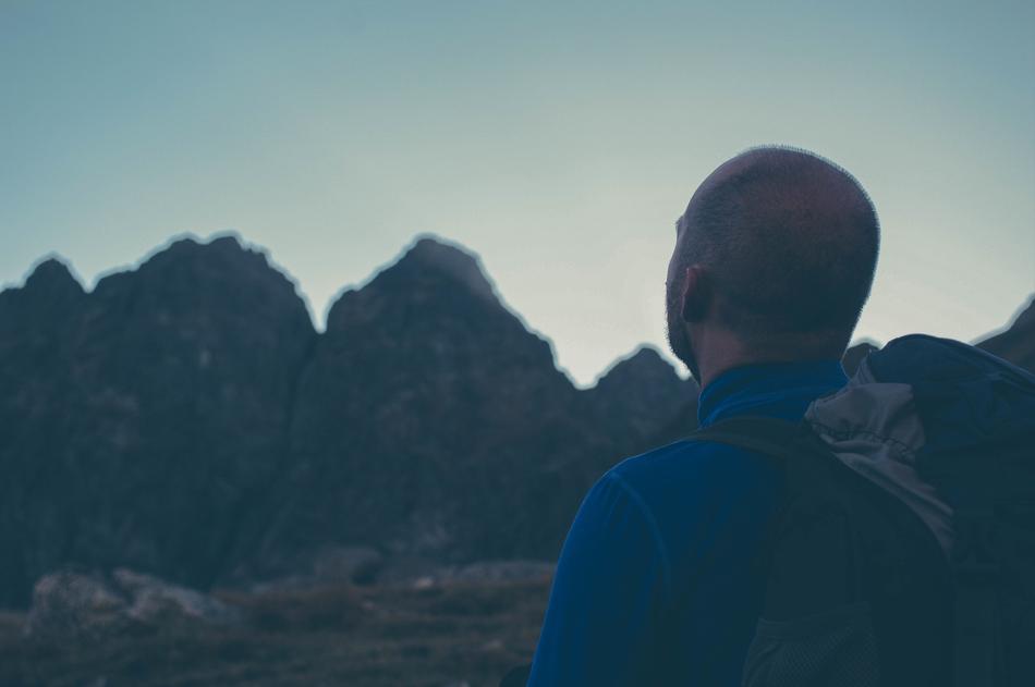 pensive man with a backpack in the mountains at dusk