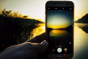 Person taking a photo of the beautiful lake at colorful sunrise, on smartphone