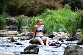 girl in bikini is sitting on a boulder in the river