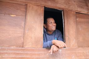 adult Batak Man looking out wooden window