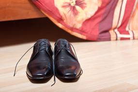 Shiny, black shoes of a groom, near the colorful bed