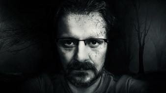 portrait of a man with glasses on a background of dark trees