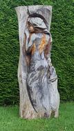 Close-up of the beautiful and colorful sculpture of the girl, in the wood, near the green plants