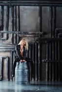 photo of a girl in a leather suit sitting on a metal barrel