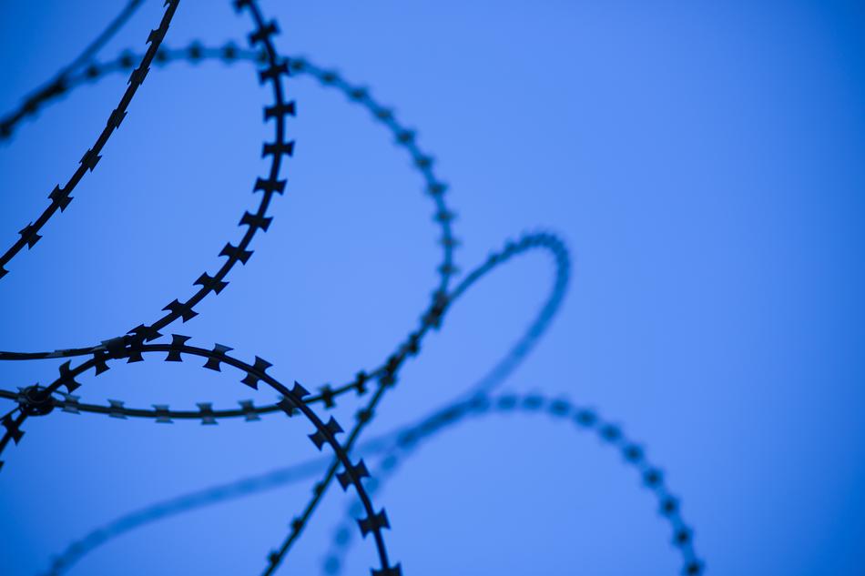 Close-up of the barbed wire with silhouettes, at blue background
