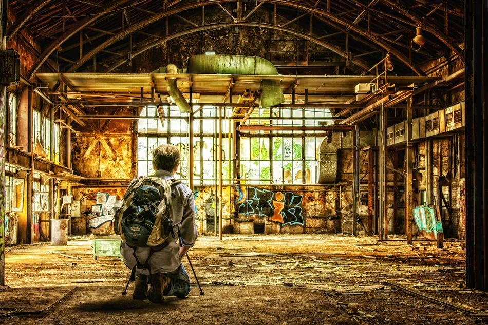 Photographer with the backpack, among the old, colorful factory building, with the colorful graffities and windows with the light