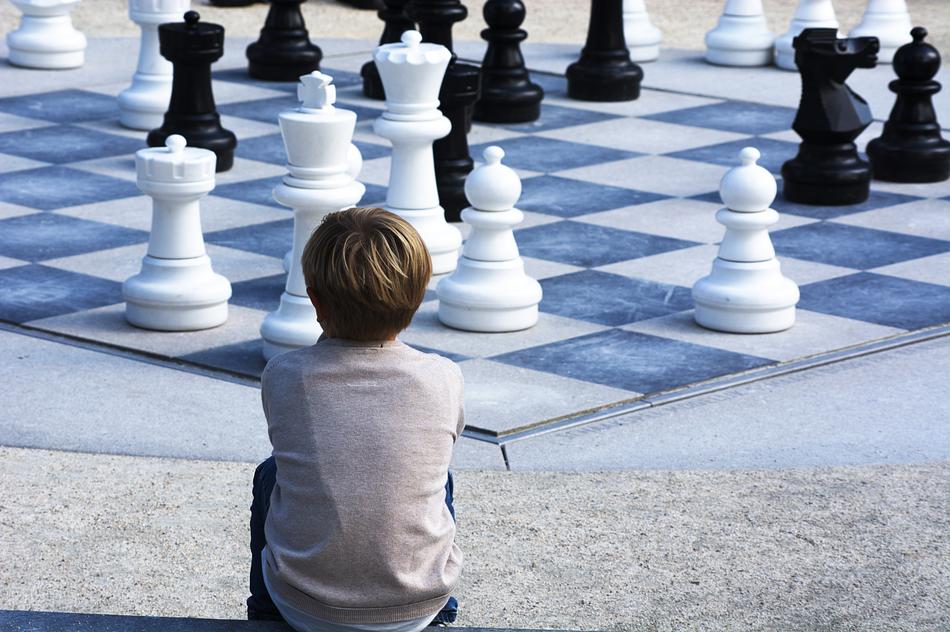 child Boy sits in front of Chessboard with figures
