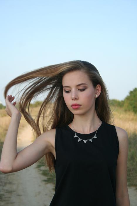 Portrait of the beautiful girl with long hair and make-up, with the necklace, on the path, among the colorful and beautiful plants