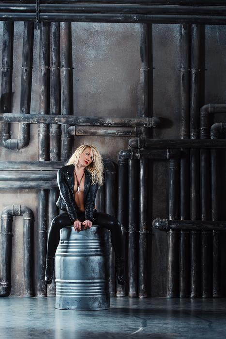 photo of a girl in a leather suit sitting on a metal barrel