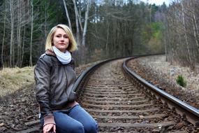 blonde Girl sits on railway in forest at fall