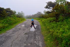 Girl running on the road, with the water puddles, among the beautiful and colorful plants