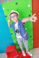 Boy in glasses and hat, standing near the colorful wall